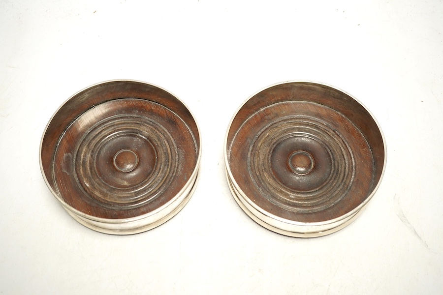 A pair of 19th century Continental white metal wine coasters, inset with turned mahogany bases, 12.5cm diameter. Condition - fair